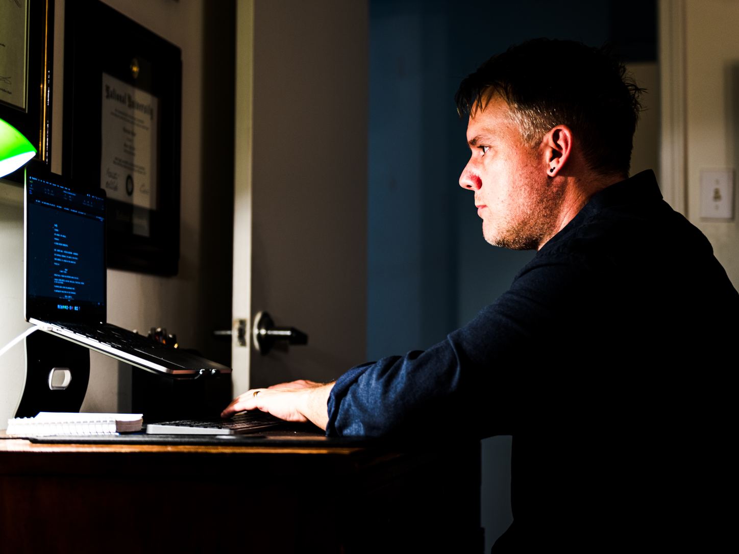 Christopher Shank in profile at his laptop, working in a dark room.