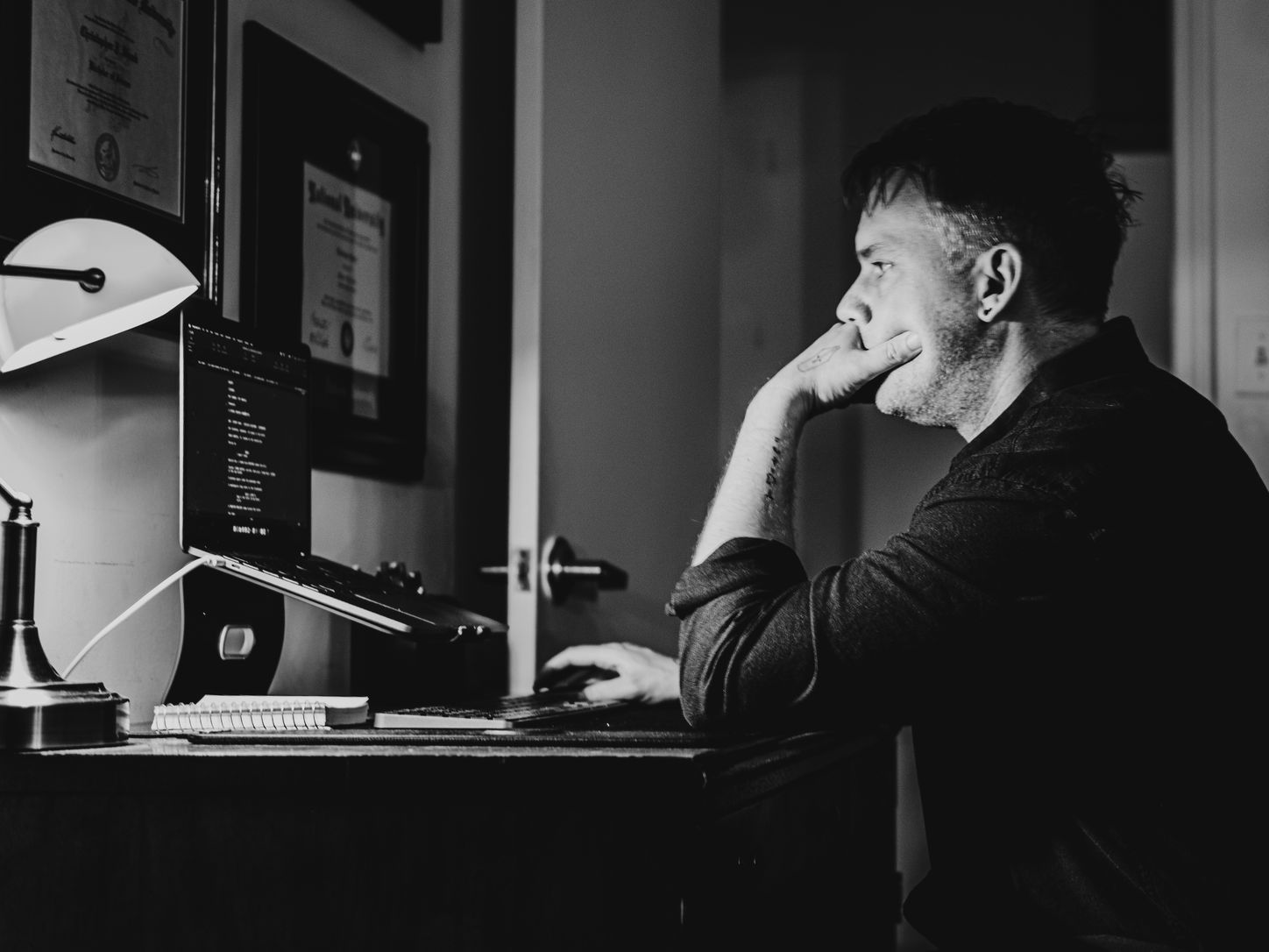 Christopher Shank at his desk in lamplight, reading a page on his laptop.