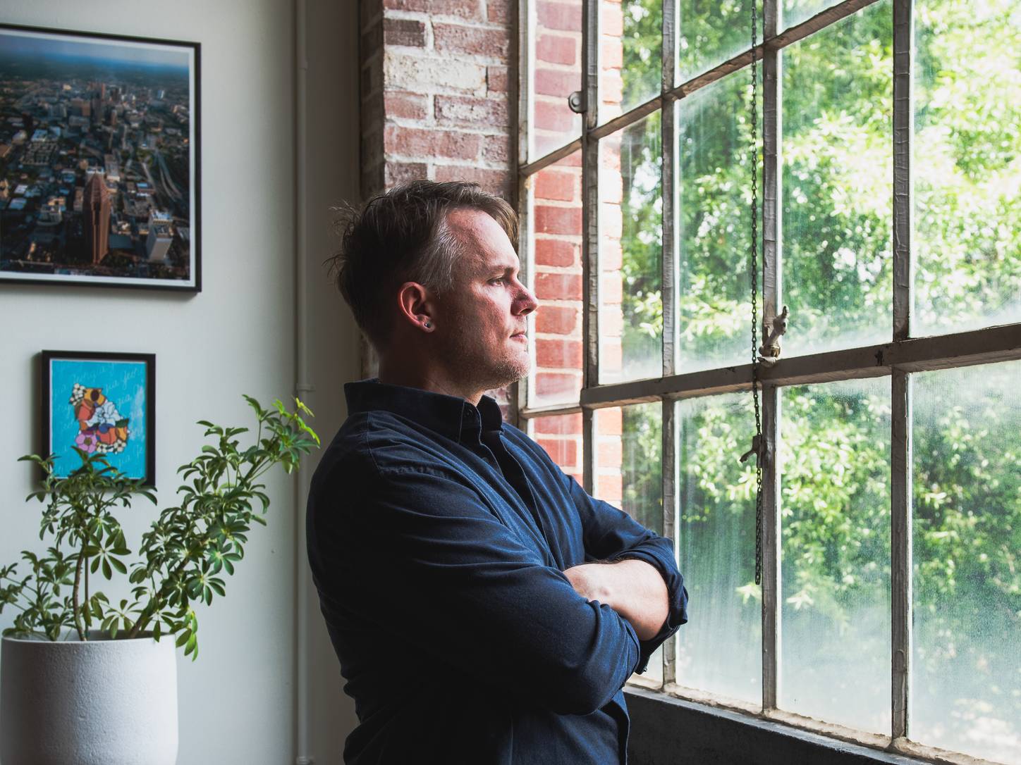 Christopher Shank standing with his arms crossed beside a tall factory window.